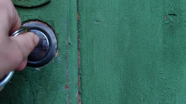 woman inserts a key into a round metal door lock on a weathered green wooden gate, access control, home security, rustic property entrance