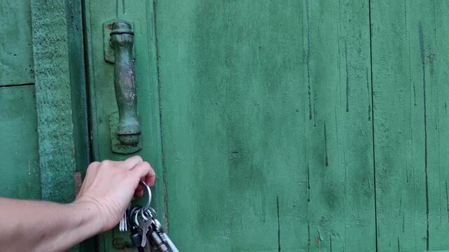 woman turns a key in the lock of a weathered green wooden gate, door, access control, home security, rustic property entrance, outdoor detail.