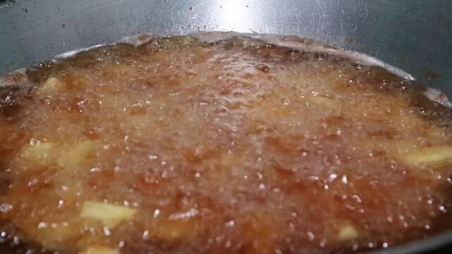 Close up view of food being deep fried in hot bubbling oil in a pan.