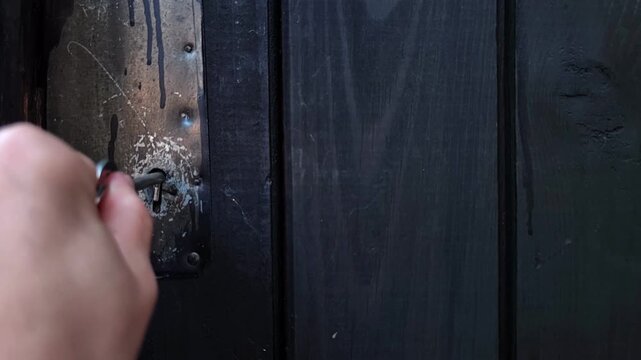 woman inserts a key into an old dark wooden door lock, rustic locking mechanism, property security, vintage entrance, close up.