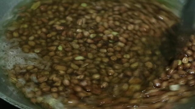 Peanuts being deep fried in hot oil inside a metal wok.
