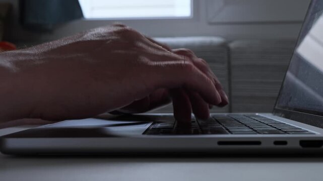 Man typing on laptop keyboard in a dark room, late night remote work