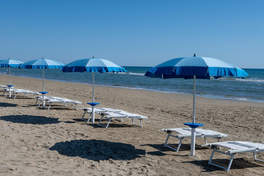 Blue beach umbrellas and empty sunbeds line on sandy shore near Sperlonga, Italy, paid beachfront, relaxation and seaside leisure in Italy
