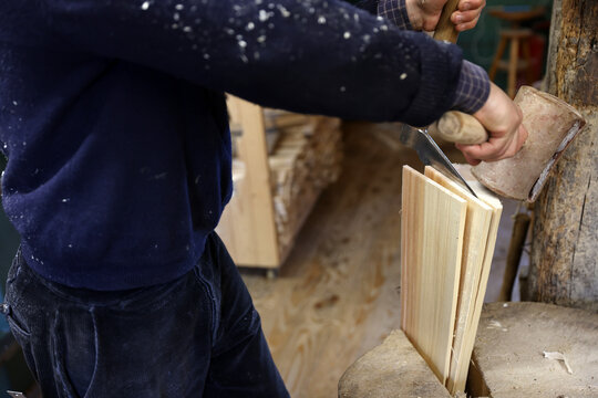 Craftsman splitting spruce wood with a froe and wooden mallet to make traditional tavaillons in the Haut-Jura, France