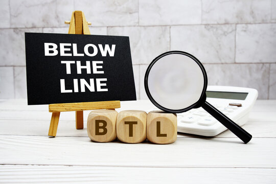 BTL Below The Line text with calculator magnifying glass and on wooden background