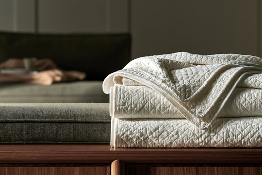 Stack of soft quilted blankets folded neatly on a dark wooden bench in a cozy living room