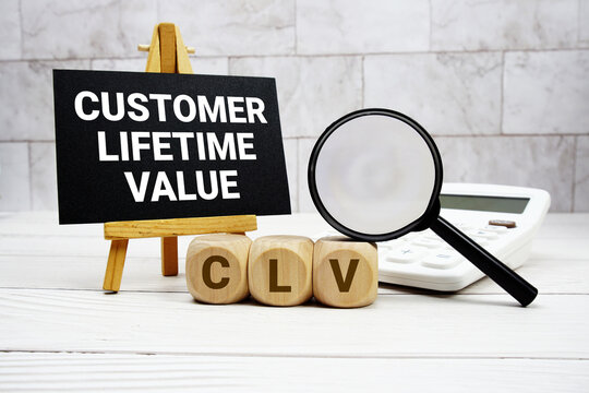 CLV Customer Lifetime Value text with calculator magnifying glass and on wooden background