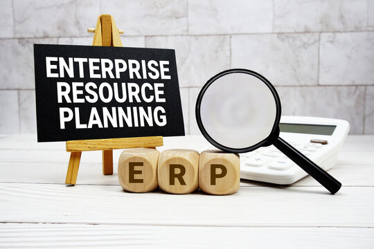 ERP Enterprise Resource Planning text with calculator magnifying glass and on wooden background