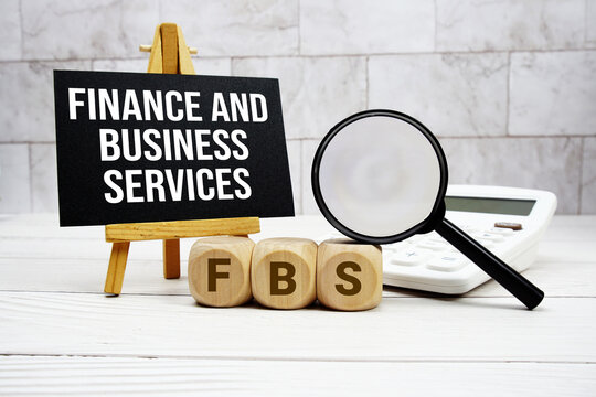 FBS Finance and Business Services text with calculator magnifying glass and on wooden background
