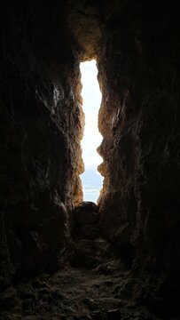 Vertical shot of a rugged stone loophole window inside a dark medieval cavern fortress