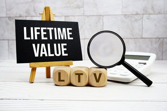 LTV Lifetime Value text with calculator magnifying glass and on wooden background