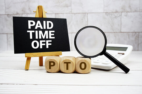 PTO Paid Time Off text with calculator magnifying glass and on wooden background
