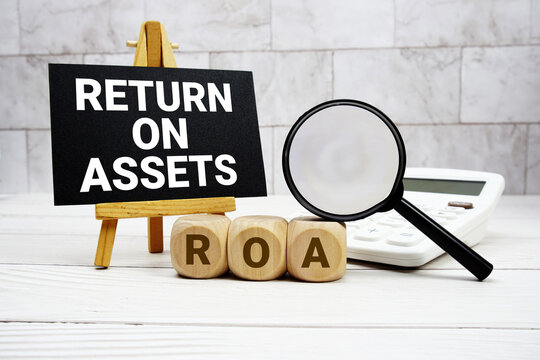 ROA Return On Assets text with calculator magnifying glass and on wooden background