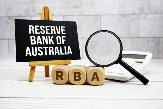 RBA Reserve Bank of Australia text with calculator magnifying glass and on wooden background