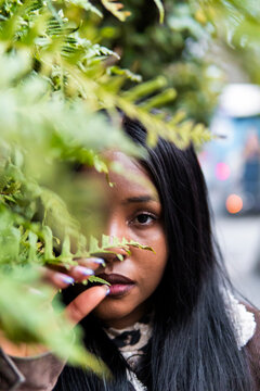 African woman peer through foliage in an urban setting