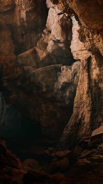Visitors explore a large cave with unique rock formations. Natural light filters through the opening, creating shadows and highlighting the textures of the rocks.