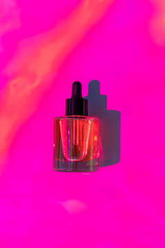 Cosmetic facial serum bottle with dropper on pink background