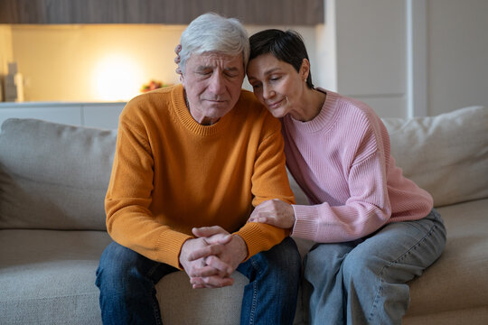 Elderly couple sitting on couch together embracing and supporting each other during difficult time, smiling tranquil woman hugging emotionally tired husband, loving spouse consoling partner on sofa.