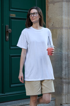 Woman in glasses holding a pink drink and wearing a white t-shirt and shorts