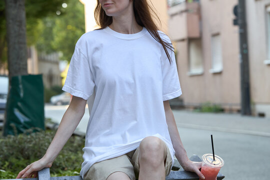 Young woman in a plain white t-shirt and shorts holding a refreshing drink outdoors