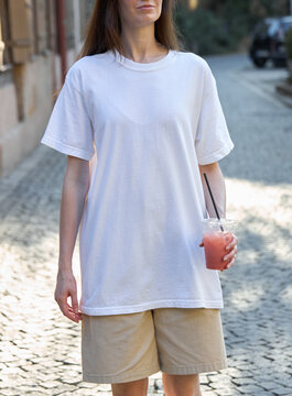 Woman in white t-shirt and shorts holding a pink drink on a cobblestone street