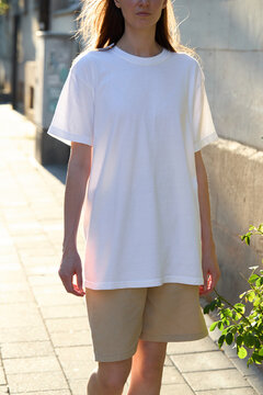 Woman in a white t-shirt and beige shorts walking on a sunlit sidewalk