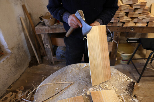 Craftsman shaping a handcrafted spruce wooden shingle (tavaillon) with a traditional broad axe in the Haut-Jura, France