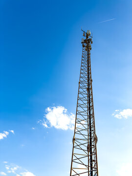 Cell tower against blue sky in daylight. A tall cell tower stands against a clear blue sky with a few clouds.