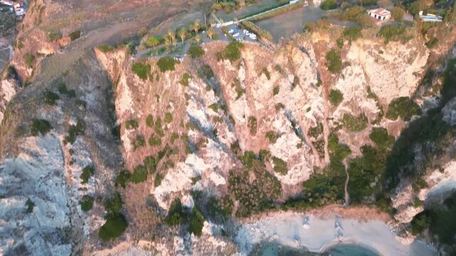 Capo Vaticano, Calabria, Italy. Aerial drone reveal of secluded turquoise coves and sunlit cliffs above the Tyrrhenian Sea on the Costa degli Dei at golden hour.