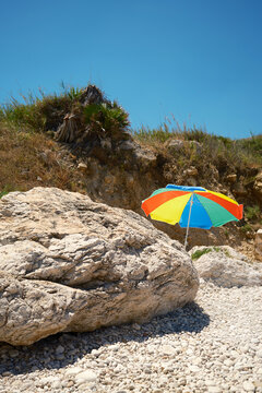 Colorful beach umbrella on a rocky Sicily shore in summer