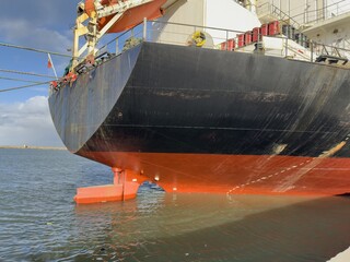 Stern of a large cargo vessel showing its orange rudder and propeller area docked at a commercial maritime port. © Iryna