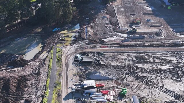 High angle drone shot of a large muddy construction site showing earthmoving equipment and materials