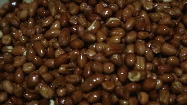 A large pile of roasted peanuts with skins on in a bowl.