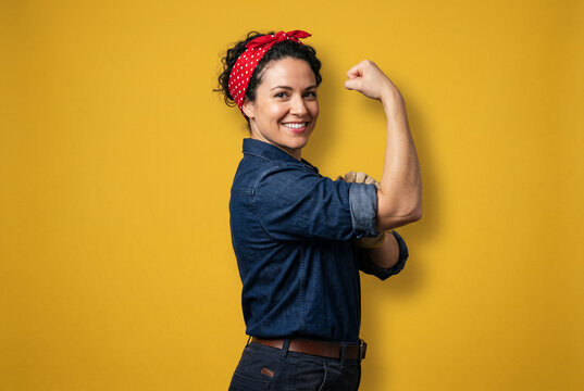 Confident young woman posing as rosie the riveter showing arm muscle