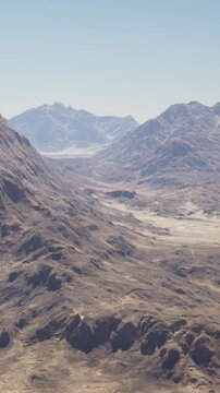 Tall mountains rise in the distance with rugged terrain. Valleys weave through the landscape under a clear blue sky. The scene shows an untouched natural setting in daylight.