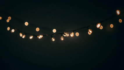 Obraz premium A string of warm glowing fairy lights hanging against a dark background, creating a soft bokeh effect for festive holiday atmosphere