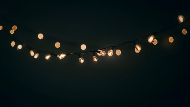 A string of warm glowing fairy lights hanging against a dark background, creating a soft bokeh effect for festive holiday atmosphere