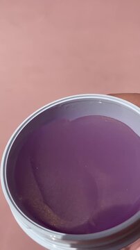 Female Hand Holding Open Jar of Lifting Purple Hydrogel Under Eye Patches with Spatula on Nude Beige Background. Skincare Beauty Routine and Cosmetic Product Application, Anti-aging skincare video