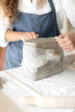 A pottery shaping clay in a studio setting with a person in an apron