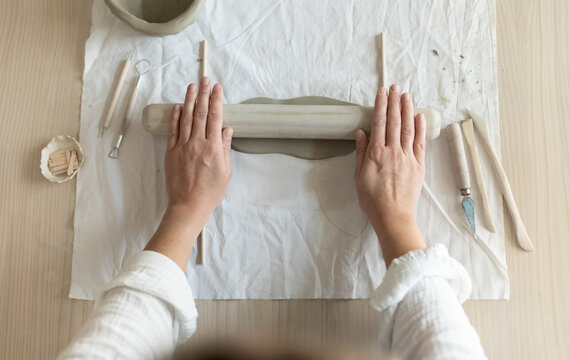 Women artist pottery shaping clay on a worktable with tools and cloth