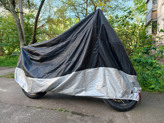 Black and gray protective cover placed over a parked motorbike standing in a residential courtyard near an apartment building © Harmony Video Pro