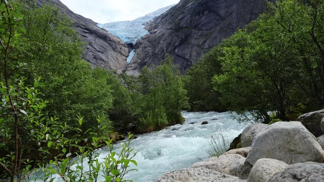 Fast flowing glacial river with view of Briksdalsbreen glacier in Norway