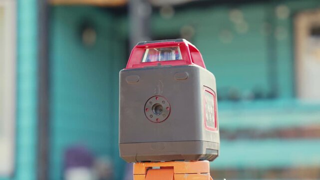 Professional laser level measuring instrument turning and scanning the surrounding area on a construction site, providing precise leveling for building works with a bright red beam