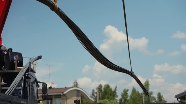 Industrial crane arm carefully lifting a heavy bundle of steel reinforcing bars at a construction site against a clear blue sky