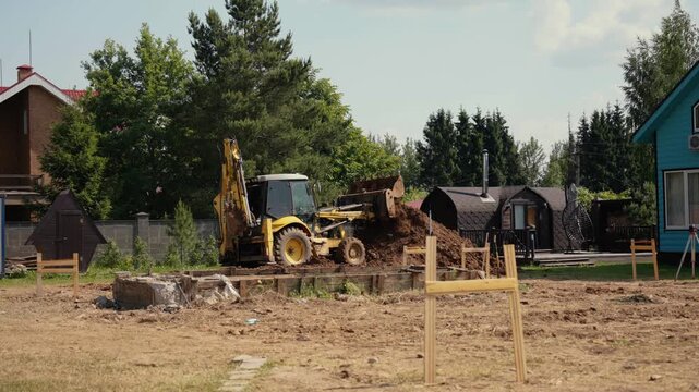 Earthmoving equipment preparing a residential plot for new building construction. Heavy machinery digging and grading the land, leveling the ground for a future home foundation in a suburban area