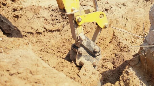 Heavy machinery with a mechanical shovel digging a hole in the ground during earthmoving works at a construction site, preparing the foundation for a new building in sunny daylight