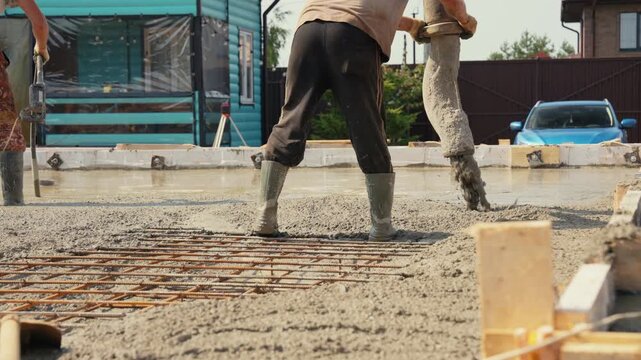 Professional construction workers pouring wet cement from a pump hose to create a reinforced concrete slab for a building foundation at a construction site on a sunny summer day
