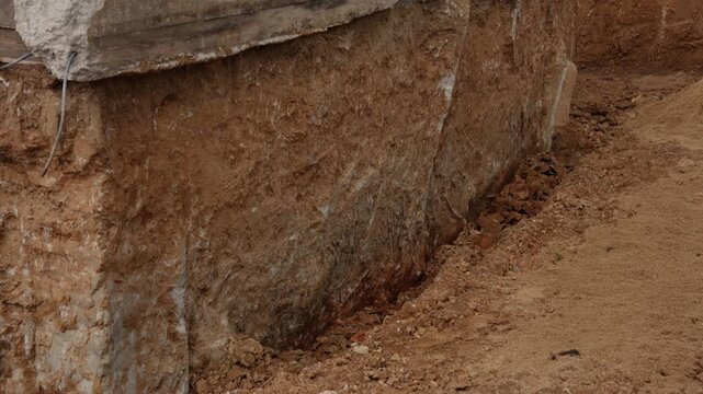 Large reinforced concrete beam lifting during foundation excavation at a building demolition site. Earthmoving machinery performing heavy work with soil, sand, and dirt in a deep trench