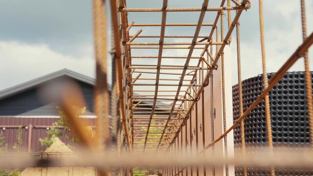 Rusted steel rebar framework providing a strong base for a future concrete foundation at an industrial construction site, with buildings and a cloudy sky visible in the background