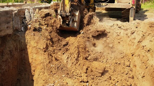 Heavy machinery excavating earth and demolishing old concrete foundation during groundwork operations on a sunny day. Construction equipment digging a deep pit for new building foundations